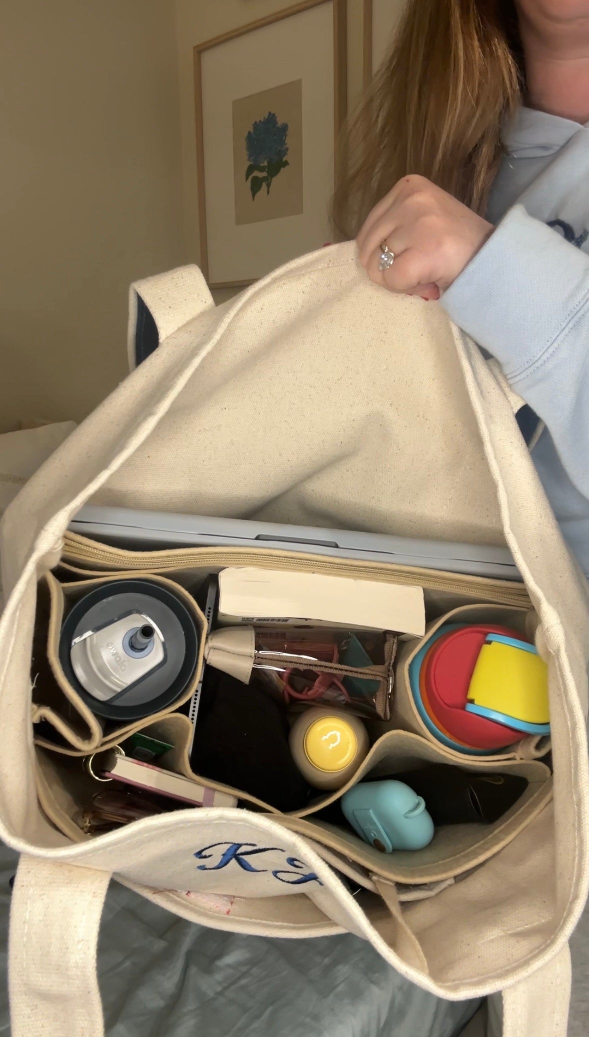 Interior view of a personalized canvas tote bag packed with daily essentials including a laptop, water bottle, book, and organizer inserts – showcasing the spacious, organized capacity of the embroidered tote from Kits Threads.