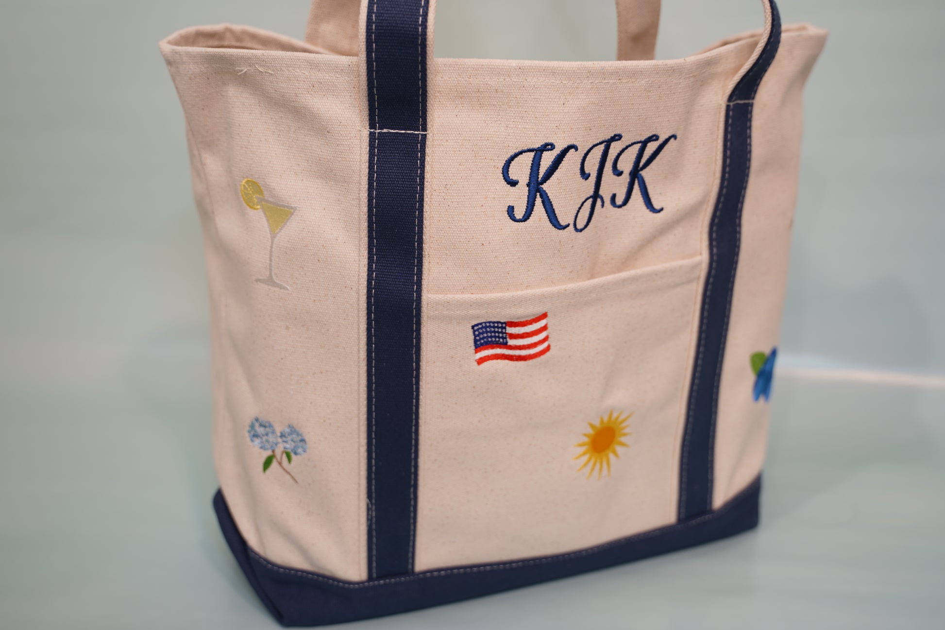 Side angle of personalized canvas tote bag showcasing embroidered monogram and summer-themed icons.
